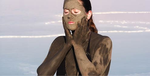 Young adult Israeli woman enjoying the natural mineral mud sourced from the dead sea, Israel. The Dead Sea known for its healthy minerals and as the lowest point on earth.(1,300 feet below sea level) 