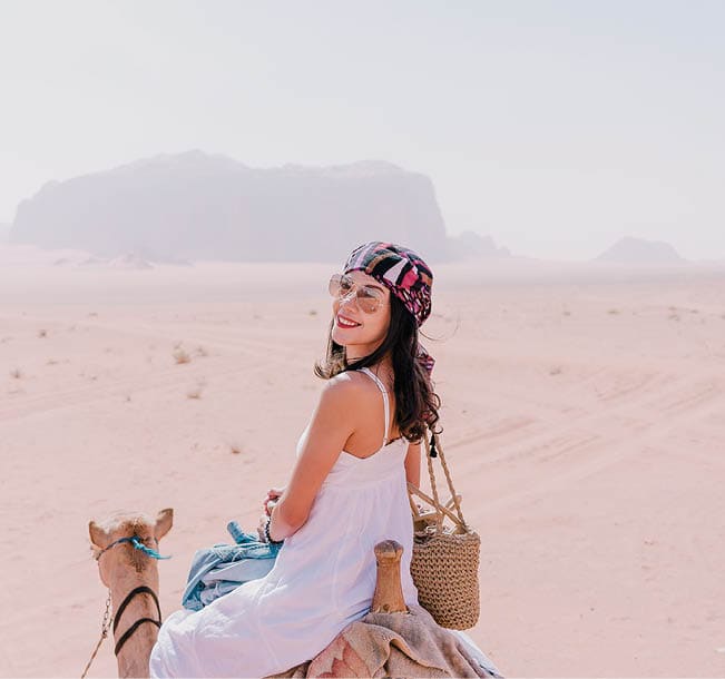 Asian young woman tourist in white dress riding on camel in wadi rum desert, Jordan