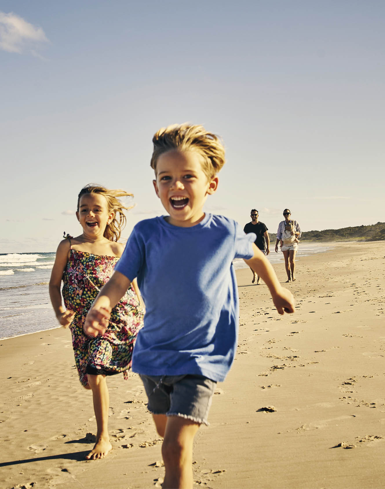Shot of two adorable little children running at the beach with their parents in the background