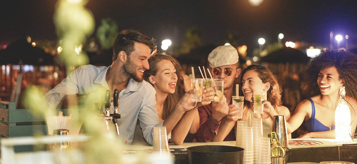 Happy friends cheering and drinking cocktails at beach party outdoor - Young millennials people having fun at weekend summer night - Youth lifestyle and nightlife concept - Main focus on left guys