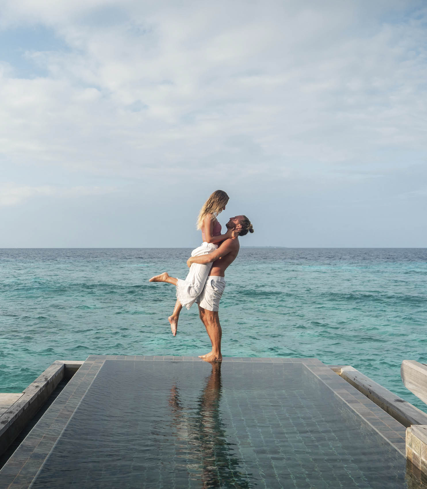 Couple enjoying tropical vacations from the edge of an infinity pool in private over water villa. People travel luxury holidays