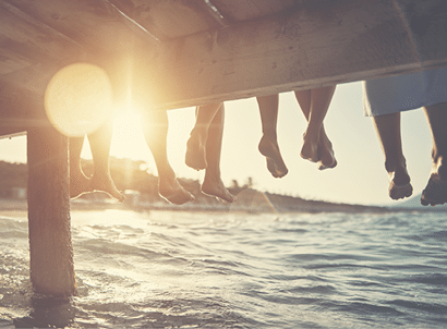 Five people having fun sitting on pier. Feet shot from below the pier. Sunny summer day evening. Nikon D850