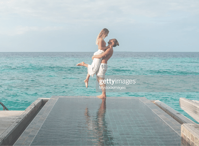 Couple enjoying tropical vacations from the edge of an infinity pool in private over water villa. People travel luxury holidays