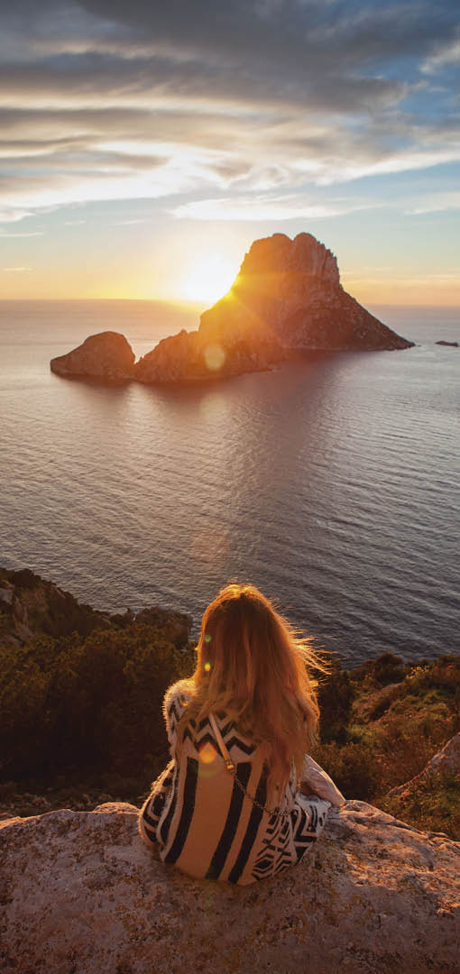 Woman back to the front watching a beautiful sunset at the beach. The beach is called Es Vedra, in Ibiza and belongs to balearic islands, in Spain