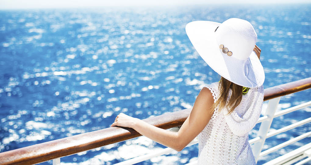 Unrecognizable woman with hat on a cruise ship looking at the view.