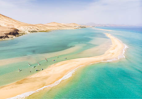 Aerial view of beach in Fuerteventura island with windsurfers learning windsurfing in blue turquoise water during summer vacation holidays, Canary islands from drone