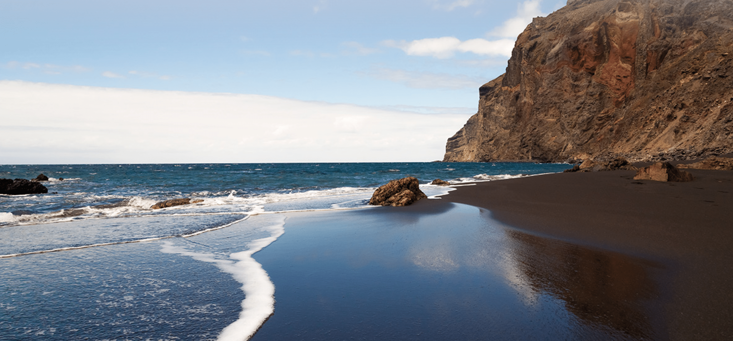 A black sand beach at the atlantic ocean at La Gomera, one of the canary islands. The sky is morrored in the wet sand.
