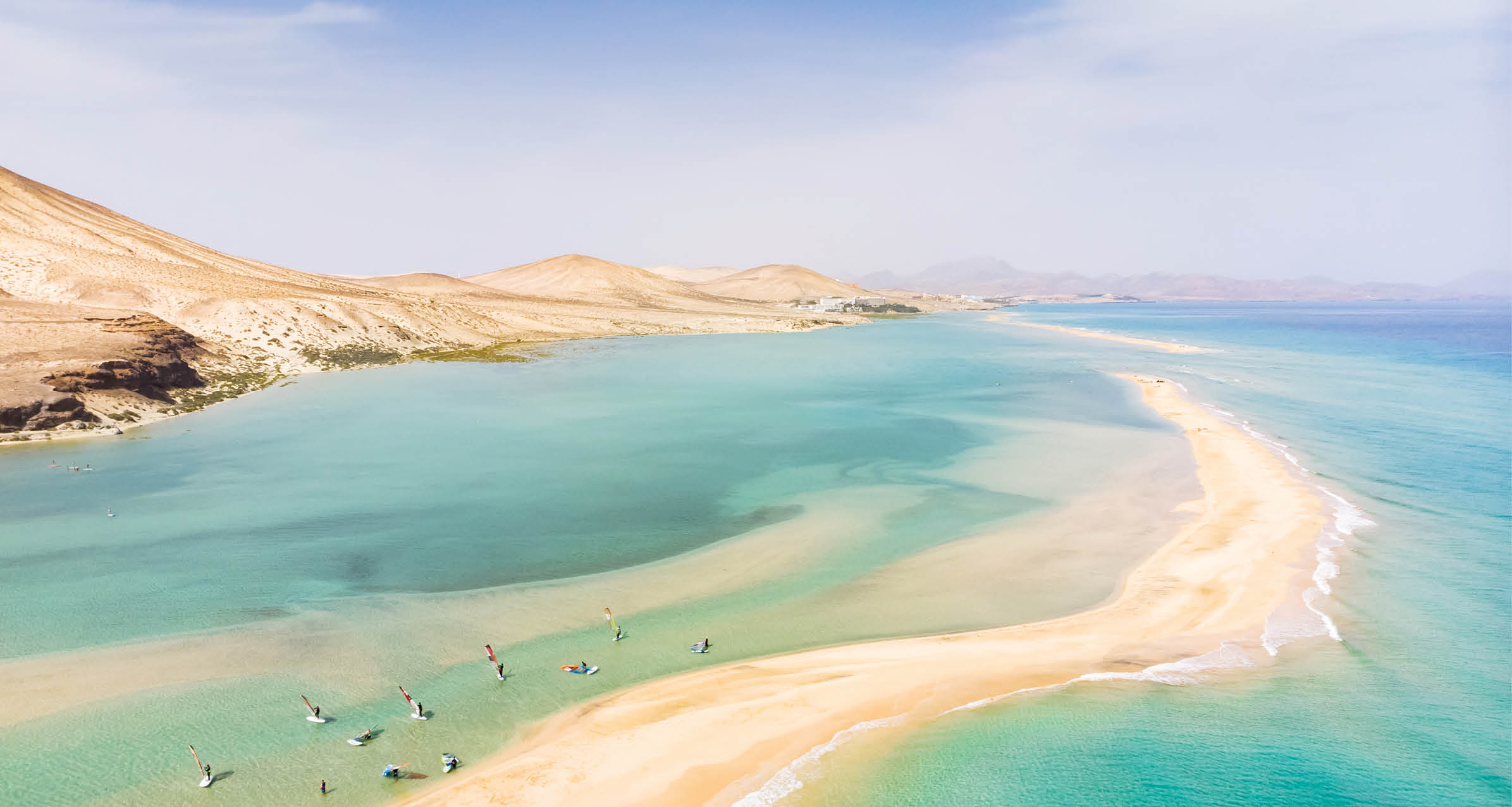 Aerial view of beach in Fuerteventura island with windsurfers learning windsurfing in blue turquoise water during summer vacation holidays, Canary islands from drone
