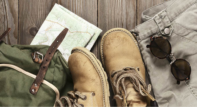 Travel accessories set on wooden background: old hiking leather boots, pants, backpack, map and sunglasses  Top view point 