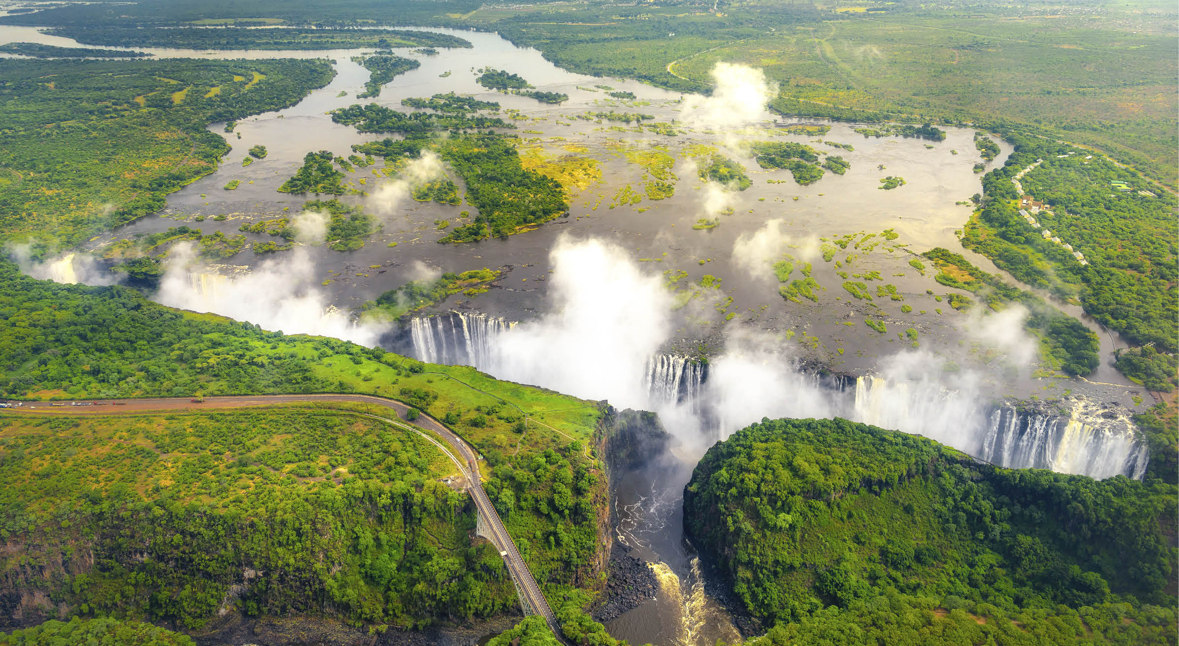 Victoria Falls in Zimbabwe and Zambia, Aerial helicopter photo, green forest around amazing majestic waterfalls of Africa. Livingston Bridge above the river