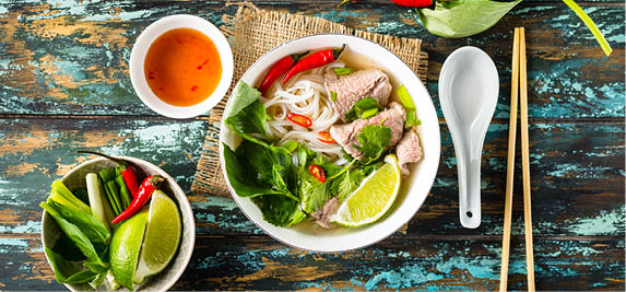 Traditional Vietnamese soup Pho bo with herbs, meat, rice noodles, broth. Pho bo in bowl with chopsticks, spoon. Space for text. Top view. Asian soup Pho bo on wooden table background. Vietnamese soup