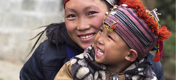 Happy Hmong woman and child smiling, sitting outside their house at Giang Ta Chai village near the hill town of Sa Pa, Lao Cai Province, North Vietnam.