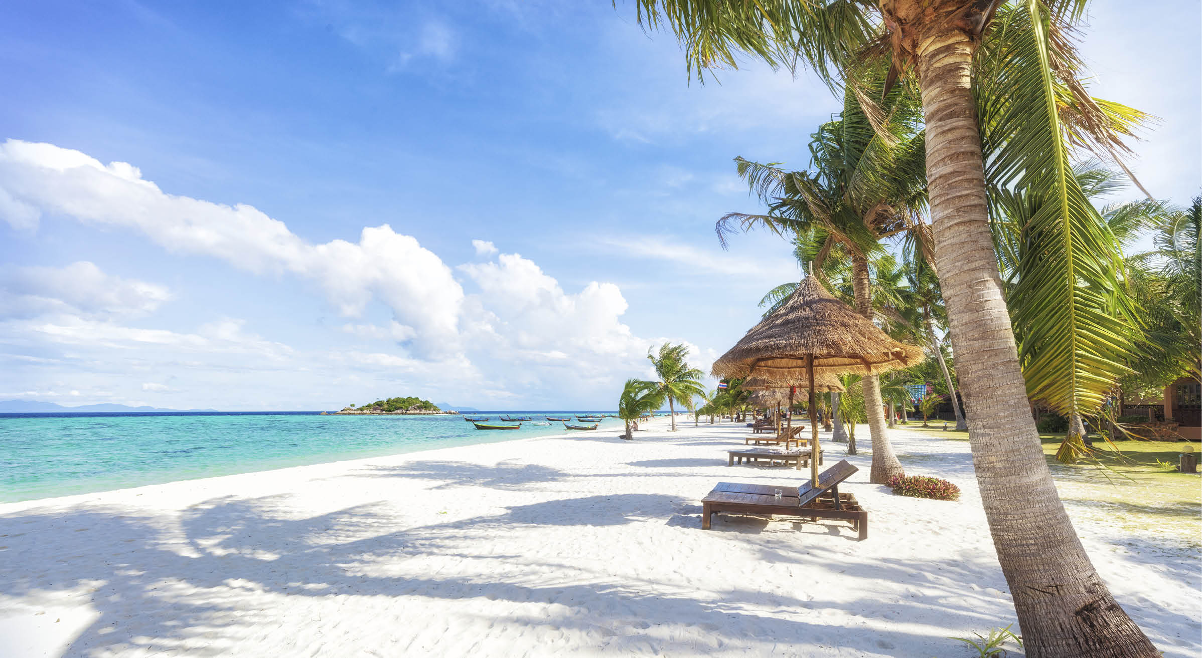 Empty sunny Koh Lipe Beach with tall palms and beach bungalows