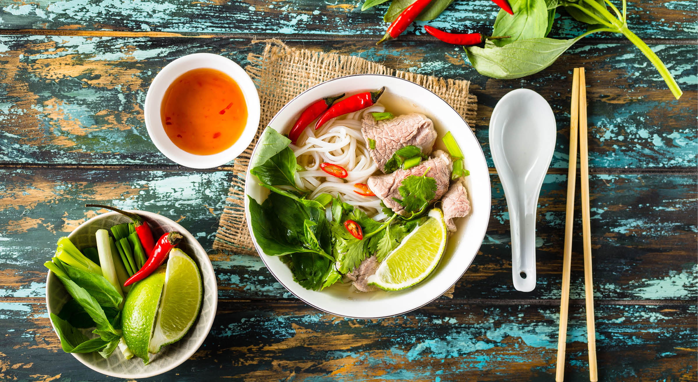 Traditional Vietnamese soup Pho bo with herbs, meat, rice noodles, broth. Pho bo in bowl with chopsticks, spoon. Space for text. Top view. Asian soup Pho bo on wooden table background. Vietnamese soup