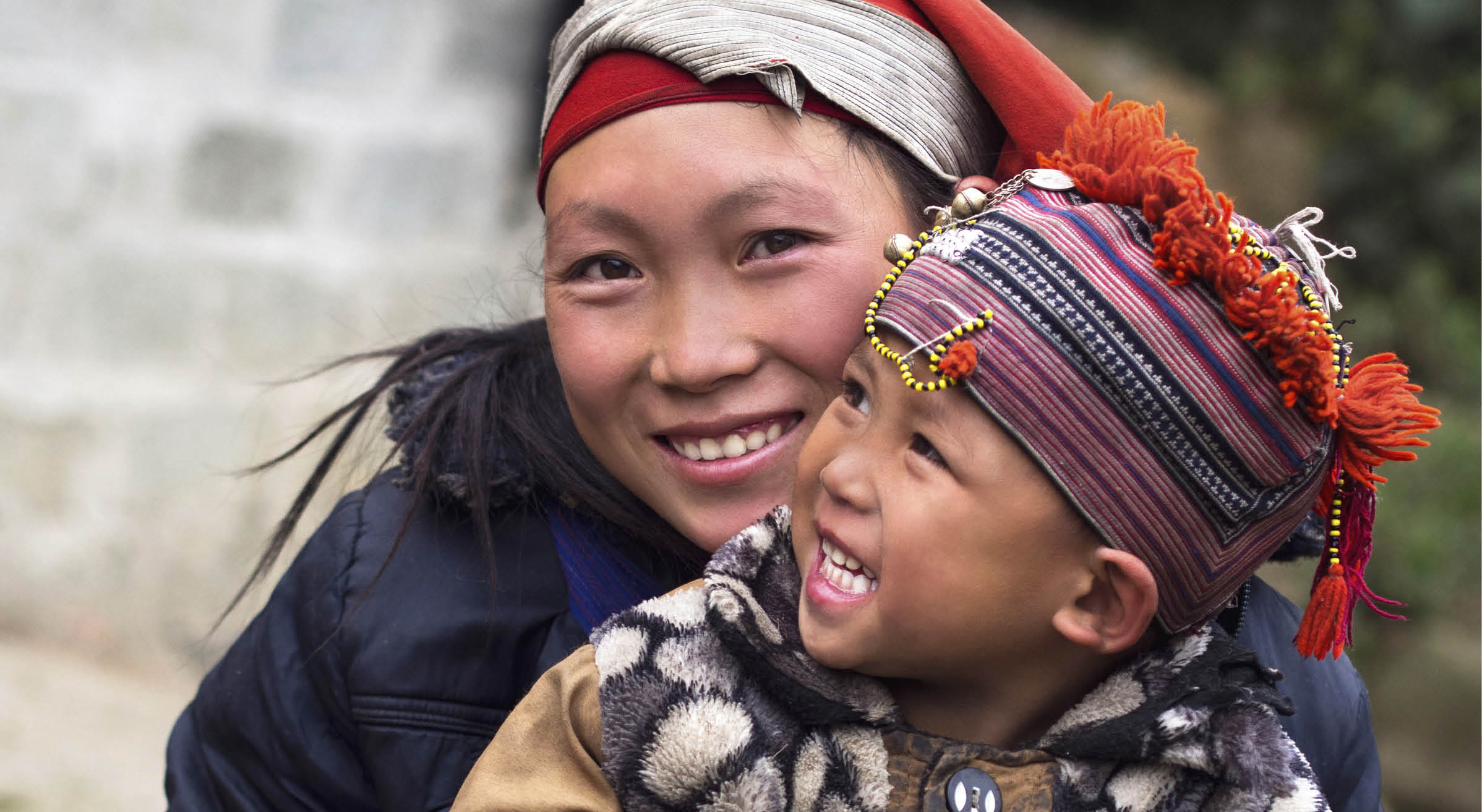 Happy Hmong woman and child smiling, sitting outside their house at Giang Ta Chai village near the hill town of Sa Pa, Lao Cai Province, North Vietnam.
