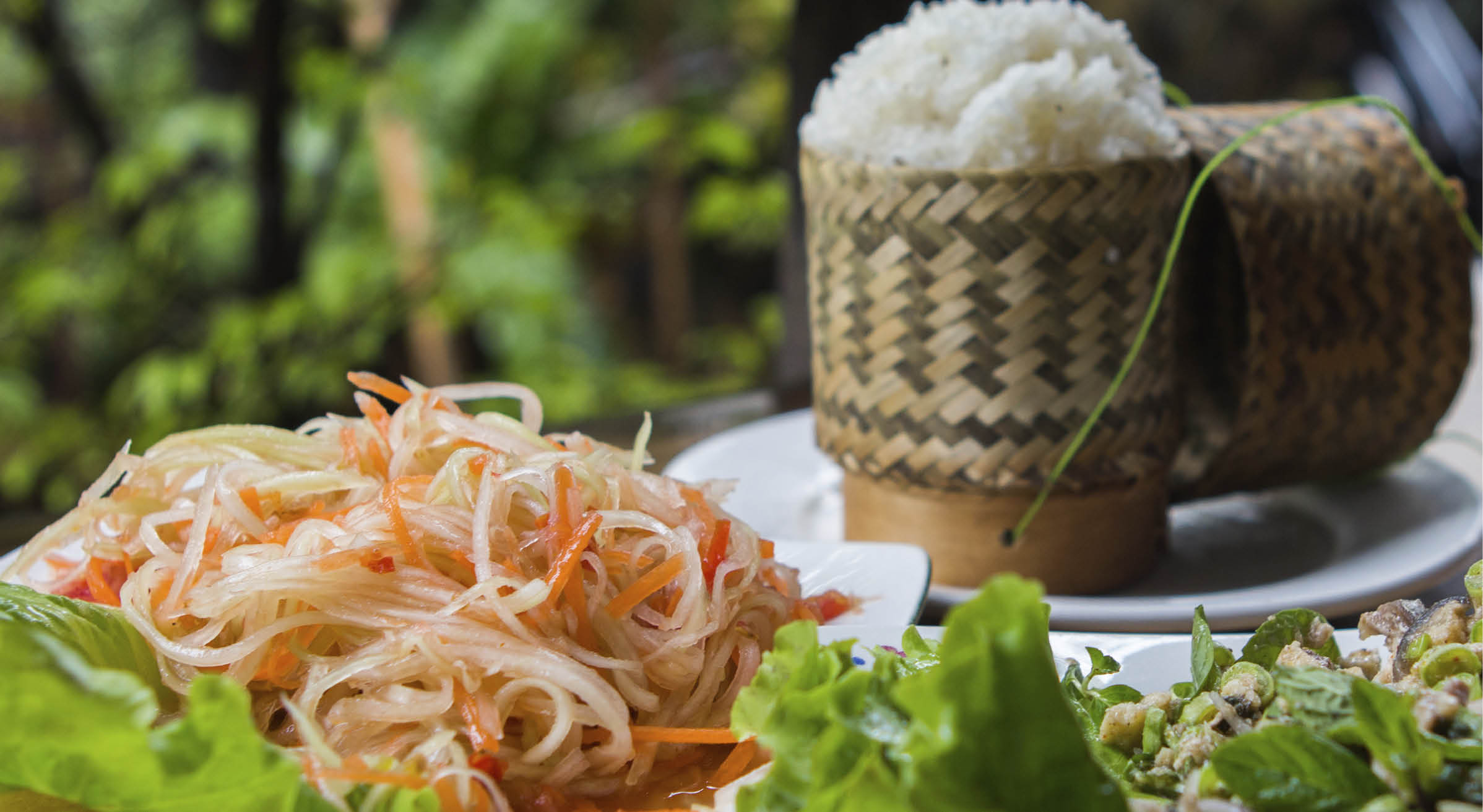 Traditional Lao cuisine: Spicy papaya salad with fish larb and sticky rice in the background. 