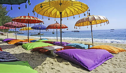 This image shows some colourful beach umbrellas and sand pillows in a pristine tropical beach bathed by the Bali sea.