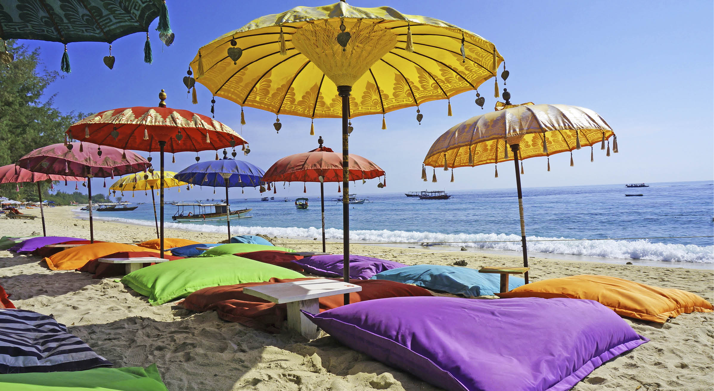 This image shows some colourful beach umbrellas and sand pillows in a pristine tropical beach bathed by the Bali sea.