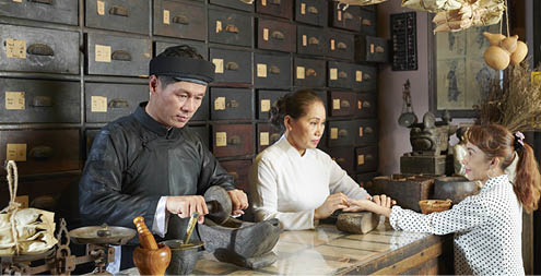 Mature Asian woman attending old Chinese drugstore to get diagnosis and buy some herbs
