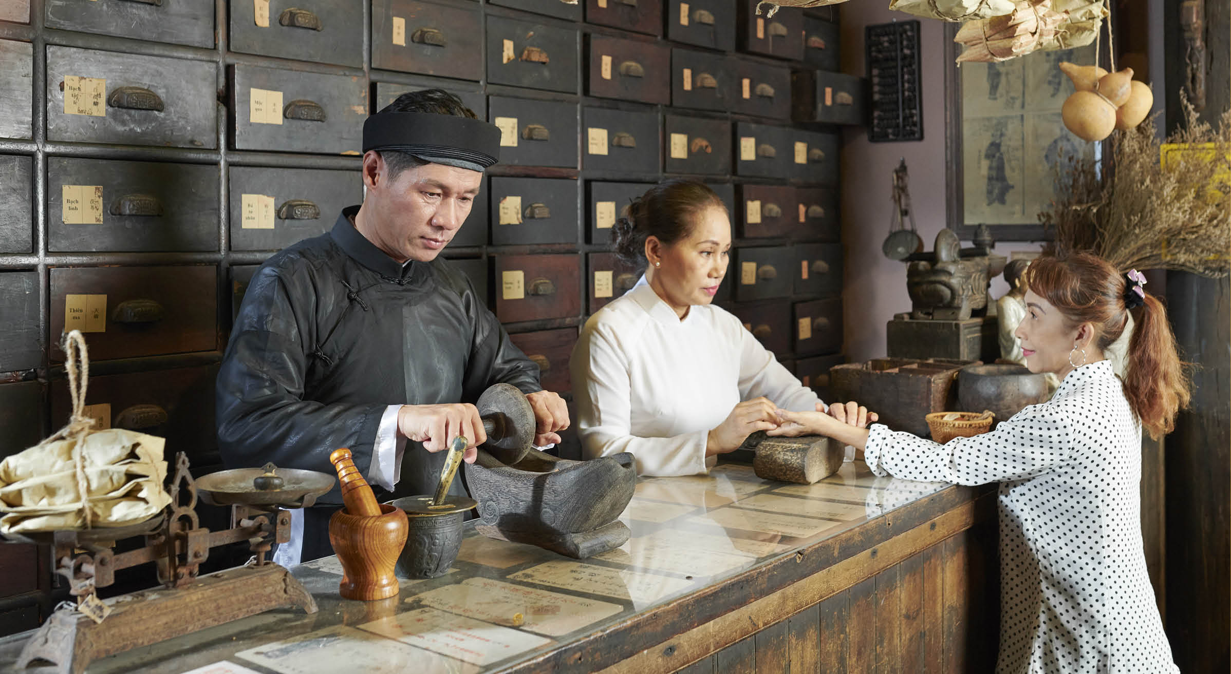 Mature Asian woman attending old Chinese drugstore to get diagnosis and buy some herbs