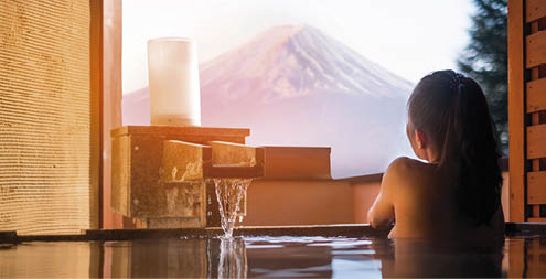 Beautiful woman enjoy onsen (mineral hot bath) in morning and seeing view of Fuji mountain in japan 