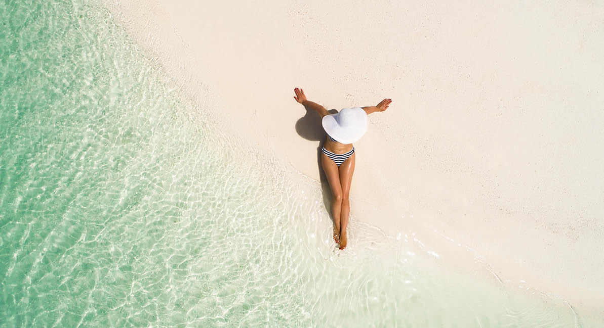 Summer holiday fashion concept - tanning girl wearing sun hat at the beach on a white sand shot from above Top view from drone  Aerial view of slim woman sunbathing lying on a beach in Maldives 