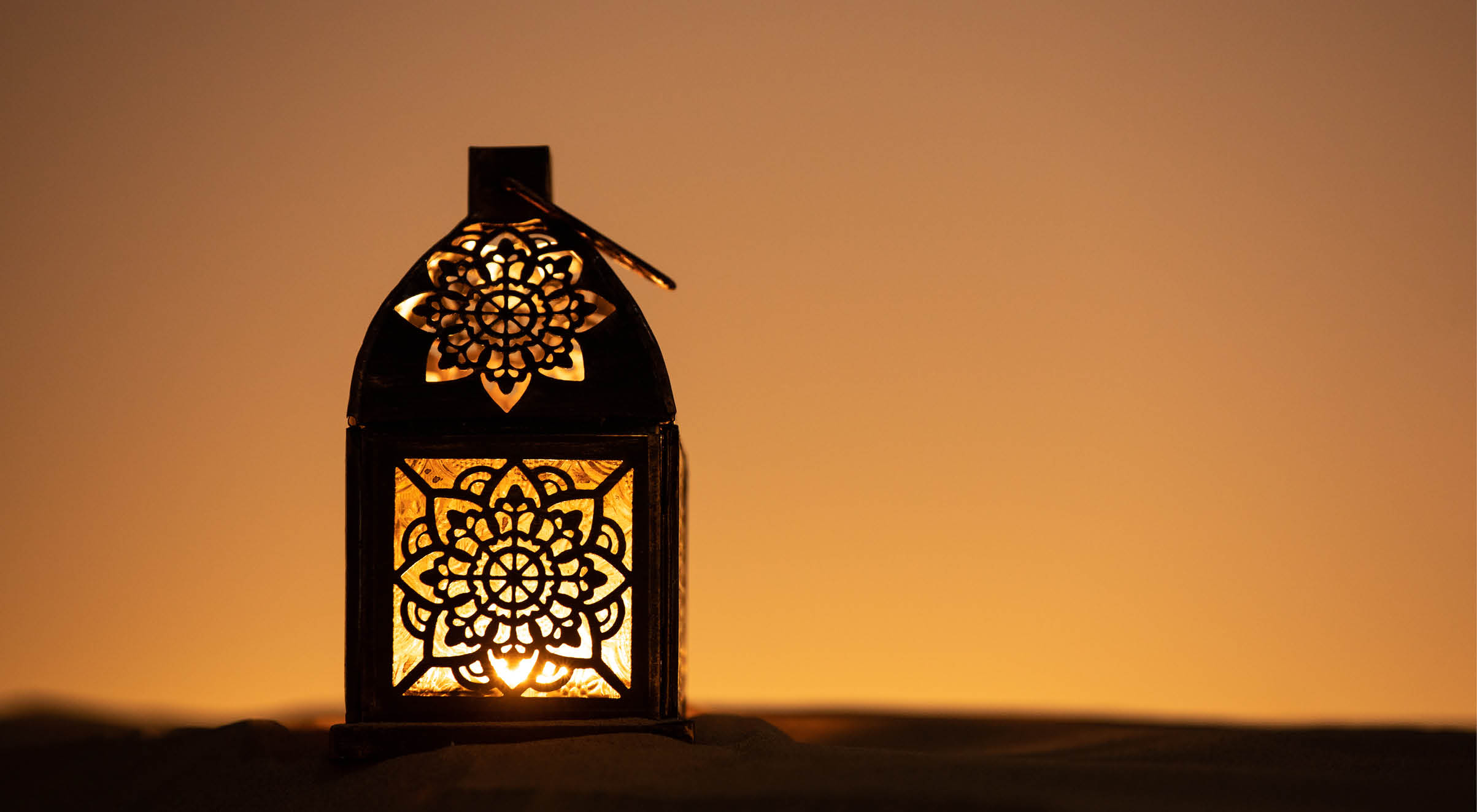 Traditional ornamental arabic lantern with a burning candle in desert after sunset during blue hour. Festivel greeting card for Ramadan Kareem and Ramadan Mubarak. Dubai, UAE.