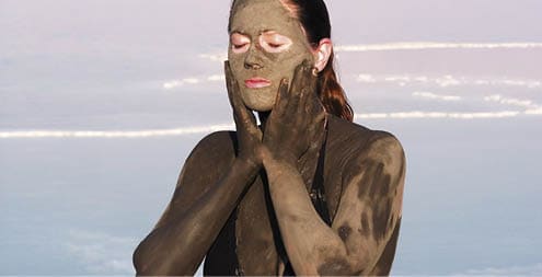 Young adult Israeli woman enjoying the natural mineral mud sourced from the dead sea, Israel. The Dead Sea known for its healthy minerals and as the lowest point on earth.(1,300 feet below sea level)