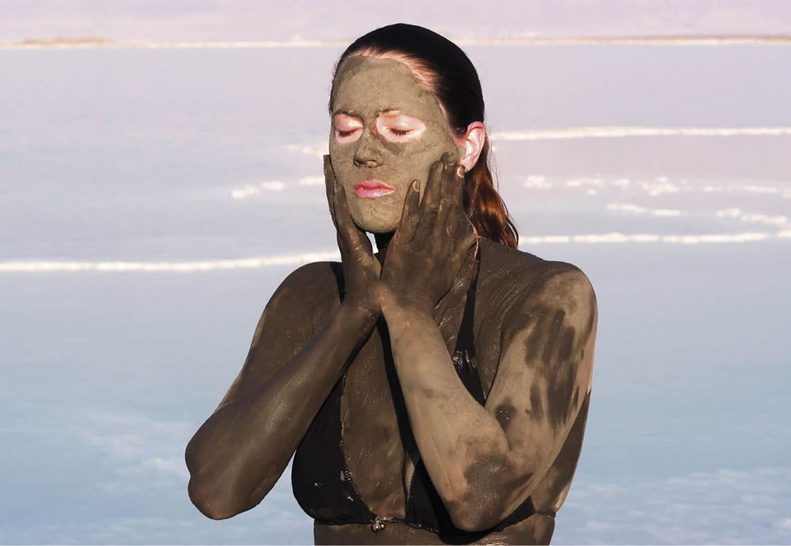 Young adult Israeli woman enjoying the natural mineral mud sourced from the dead sea, Israel. The Dead Sea known for its healthy minerals and as the lowest point on earth.(1,300 feet below sea level)