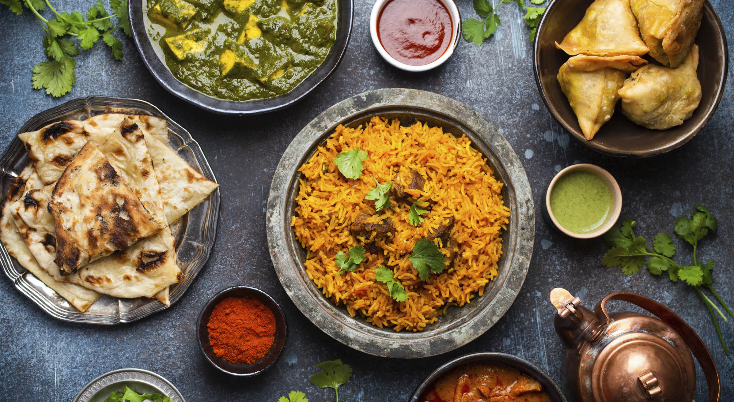 Top view of Indian traditional dishes and appetizers: chicken curry, pilaf, naan bread, samosas, paneer, chutney on rustic background. Table with choice of food of Indian cuisine, dinner/buffet