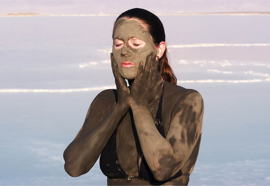 Young adult Israeli woman enjoying the natural mineral mud sourced from the dead sea, Israel. The Dead Sea known for its healthy minerals and as the lowest point on earth.(1,300 feet below sea level) 